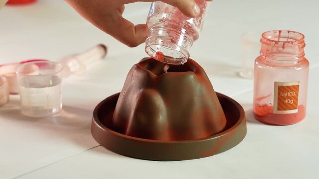 A child pours chemical reagents into a plastic Volcano. Children's chemical experiment Volcano. Effervescent reaction of soda and citric acid and water. Children's toy, experiment, learning, orange,