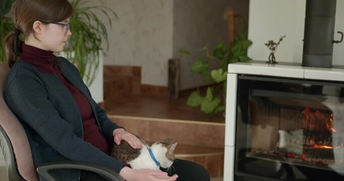 Girl Hold Kitten Tabby Cat on Laps Relaxing Near Fireplace at Home. 4K 10-bit