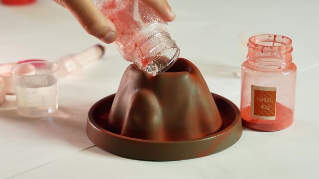 A child pours chemical reagents into a plastic Volcano. Children's chemical experiment Volcano. Effervescent reaction of soda and citric acid and water. Children's toy, experiment, learning, orange,