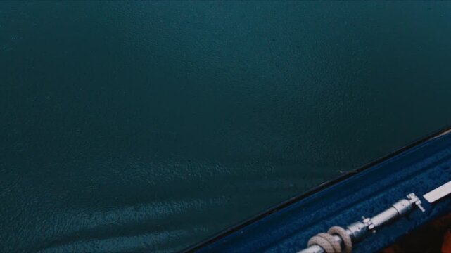 Dark water pipe over blue canal beside industrial metal infrastructure during rain with wet texture, calm surface, ripple pattern, deck rope, bridge structure, and moody coastal utility detail