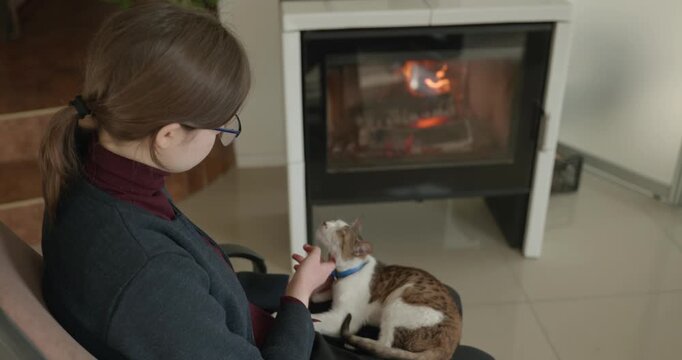 Girl Hold Kitten Tabby Cat on Laps Relaxing Near Fireplace at Home. 4K 10-bit