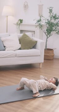Active Asian little girl practicing bridge pose yoga backbend on a mat in the living room.