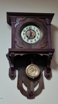 Antique wall clock with dark wood casing, cream-colored dial, and ornate brass pendulum featuring floral engravings, classic timepiece design, vintage home decor, timeless elegance concept.