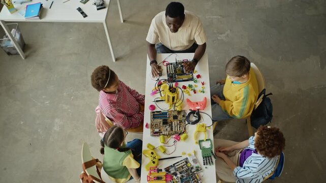 African American male teacher and multiethnic children assembling robotic models and circuit boards in modern classroom. Footage is ideal for STEM education and school promotional campaigns