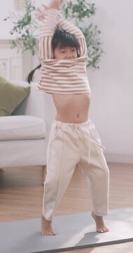 Energetic Asian cute little girl jumping with joy on a yoga mat in the living room at home.