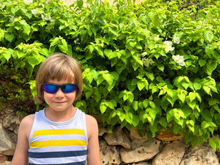 Happy 7 year old boy in tank top and sunglasses enjoying summer vacation travel. Cute schoolboy portrait during summer holidays traveling abroad in sun glasses