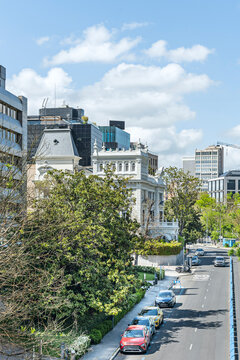  Historic ornate mansion contrasting with modern glass towers along tree-lined Madrid street with parked cars