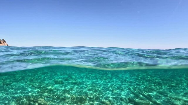 Over under view of crystal clear Mediterranean Sea water on sunny day, transparent water surface shows seabed under blue sky. Crystal clear Mediterranean Sea water split level view
