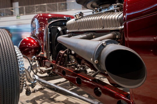 Close-up of a custom classic hot rod side exhaust system and exposed V8 engine, highlighting the tubular chassis and front suspension.