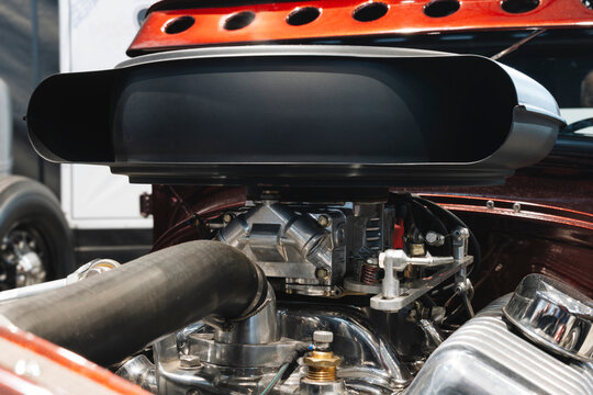 Detailed of a custom V8 engine with a high-rise air intake scoop, four-barrel carburetor, and polished finned aluminum valve covers.
