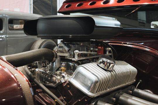 Detailed view of a high-performance V8 engine featuring a hood scoop, performance carburetor, and polished aluminum valve covers.