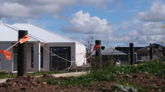 A residential construction site in Truganina, Melbourne, Australia. Drainage pipes wrapped with orange safety flagging tape mark the foreground boundary. Outer suburb housing growth.