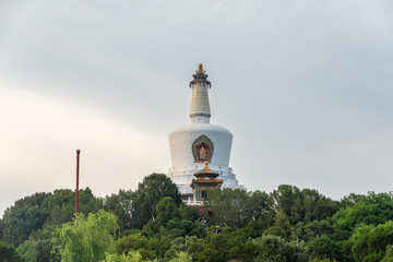 Fototapeta premium White Dagoba Stupa Rising Above Lush Green Tree Canopies at Beihai Park Under Overcast Sky at Daytime in Beijing, China