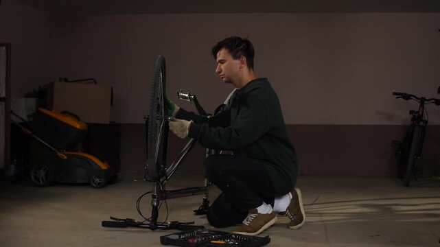 Young man assembling a bike wheel on a repair stand, performing maintenance and servicing in a home garage with a tool kit on the floor
