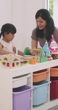 Asian little girl playing with educational wooden toys at table with her mother.