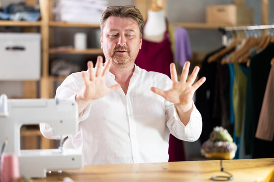 Middle-aged male tailor stretching while sitting next to sewing machine