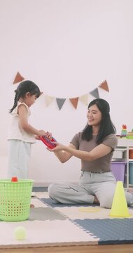 Happy Asian mother and little girl playing ring toss game together on the floor at home.