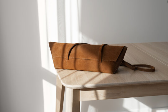 Minimalist elegant woman fashion mid-seasonal autumn accessory, sueded caramel brown baguette hand bag on neutral beige wooden table, empty neutral wall background with copy space