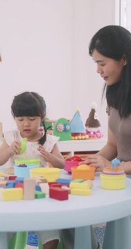 Asian mother and little daughter sorting plastic toy food into colorful bowls.