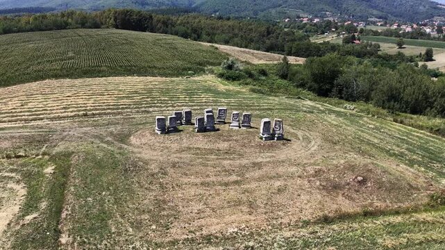 High-quality aerial drone footage of historic medieval stone tombstones located in a peaceful rural landscape surrounded by agricultural fields, rolling hills, and a small village