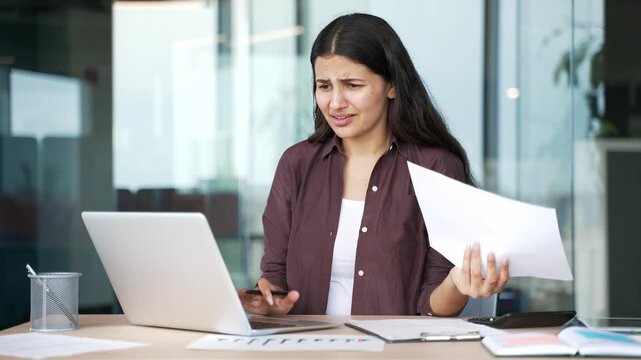 Worried businesswoman checking reports and documents on laptop while working in business office. Confused female bookkeeper faces accounting issues, calculation errors and financial discrepancies.