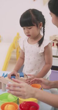 Asian little girl playing with educational wooden toys at table with her mother.