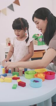 Asian little girl playing with educational wooden toys at table with her mother.