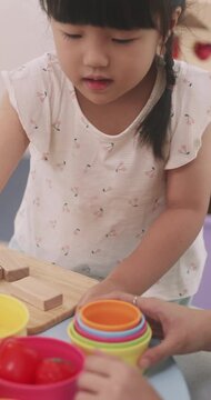 Asian mother and little daughter sorting plastic toy food into colorful bowls.