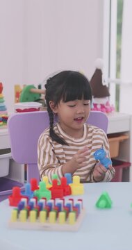 Cute little Asian girl playing educational plastic nuts and bolts toy at table.