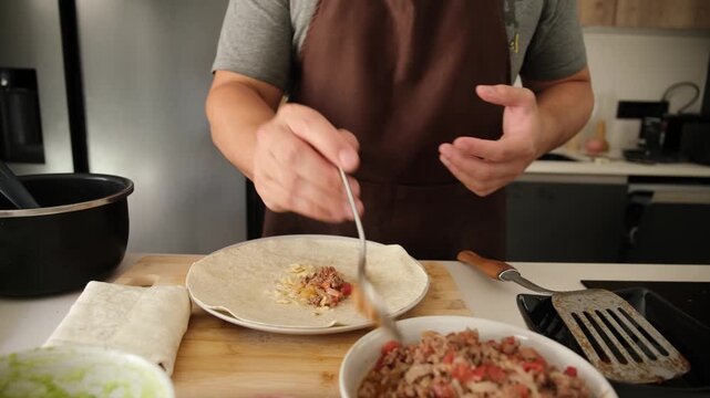 Male chef in a brown apron cooking a traditional mexican burrito in a modern kitchen at home