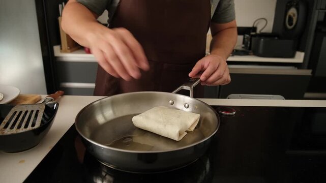 Professional chef preparing and pan frying traditional Mexican burritos on an induction hob