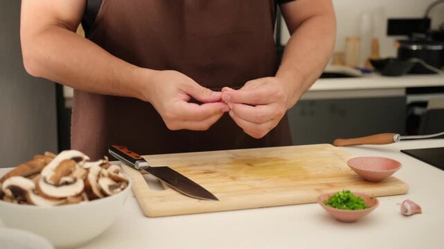Man preparing a meal by chopping fresh garlic on a wooden cutting board in a home kitchen