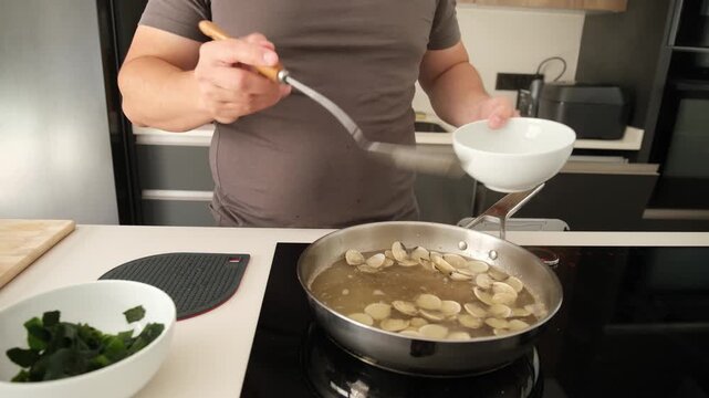 Male cook using a skimmer to take cooked clams out of a pan and putting them into a bowl