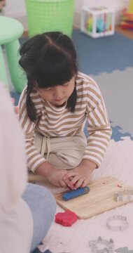 Asian little girl playing playdough with wooden hammer and tools on wooden board.