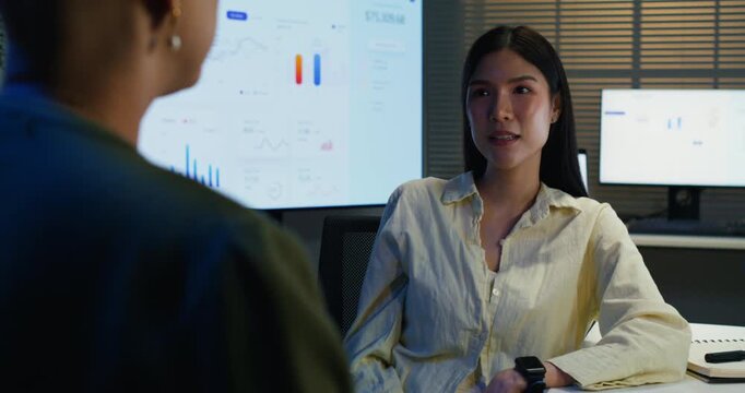 A manager mentors an overworked employee while reviewing performance charts and documents during a late office session.