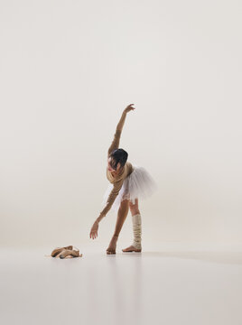 Female ballet dancer stretching toward floor beside pointe shoes in minimalist studio. Concept of flexibility practice, injury prevention, ballet conditioning.