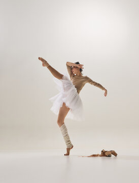 Ballerina holding dramatic balance en pointe beside ballet shoes in minimalist studio. Concept of technical mastery, performance preparation, professional dance training.