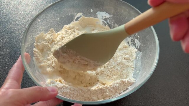 Close-up of pouring milk into a glass bowl with flour to make dough. Baking process