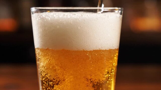 Pouring golden beer into a glass, creating foam and bubbles, close-up