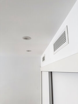 A rectangular air diffuser mounted high on a white wall in a bright apartment. Modern home ventilation system