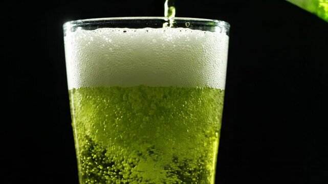 Green liquid pouring into glass creating frothy foam, refreshing beverage close-up