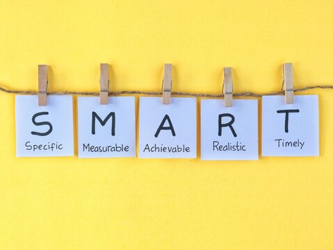 SMART (Specific, Measurable, Achievable, Realistic, Timely) handwritten on paper attached to rope string with wooden clothespins. Perfect for business strategy, management and personal development