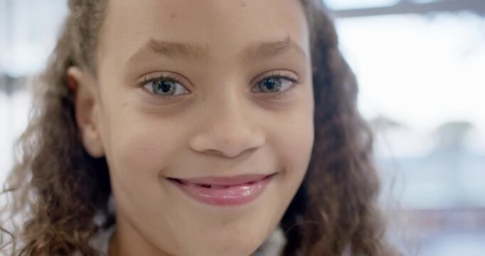 Reacting to camera's eye contact, female child smiling slowly by window, revealing missing tooth