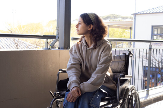 African American female youth sitting in manual wheelchair on balcony, looking left, clasping hands
