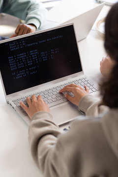 Youth students coding together at study table in library with silver laptop showing code