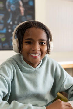 African youth male smiling and studying at desk wearing white headphones and seafoam hoodie
