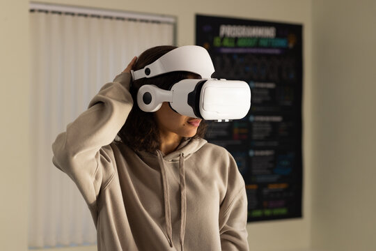 African American woman adjusting white VR headset wearing tan hoodie in lab with code poster