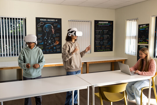 African students wearing white VR headsets gesturing in lab while classmate using silver laptop