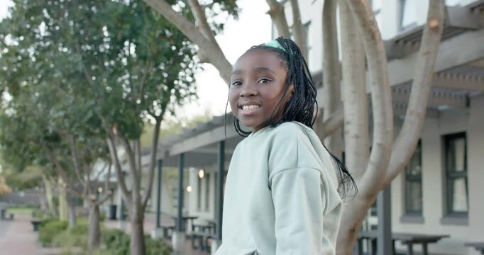 African female youth turning toward camera as framing tightening, smiling in mint hoodie by tree