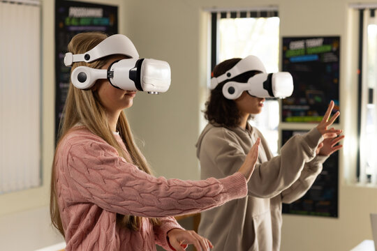 Diverse youth females wearing white VR headsets pink sweater, beige hoodie using VR in tech lab